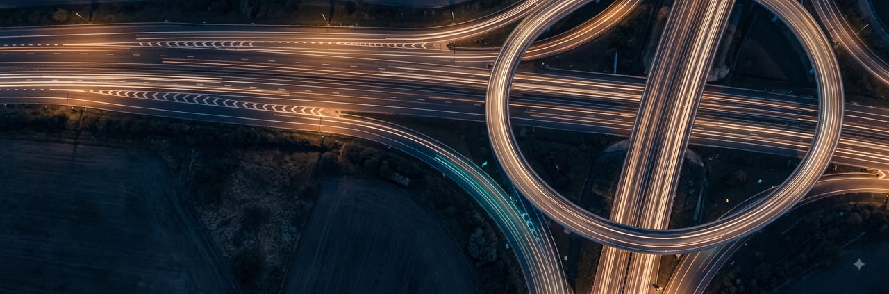 Night light-trails flowing through a motorway interchange seen from above.